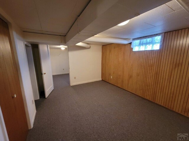 basement with wood walls, dark carpet, and baseboards