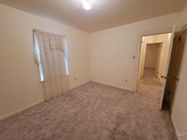 spare room with baseboards and light colored carpet