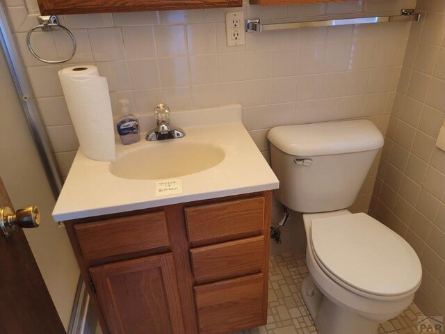 half bathroom featuring tile walls, vanity, and toilet