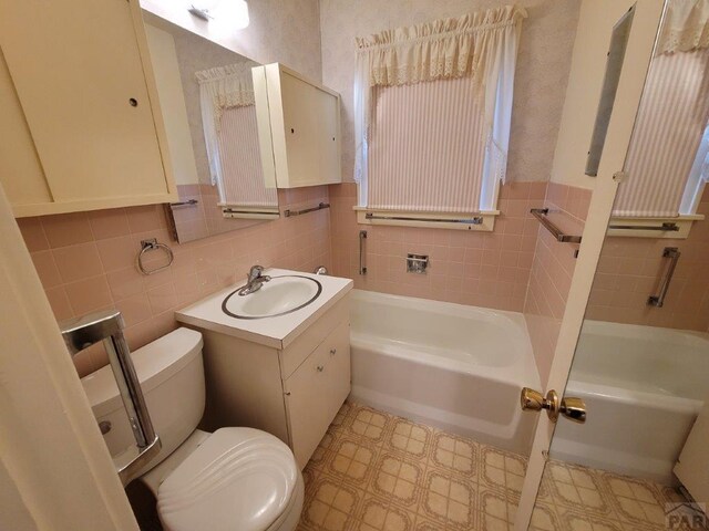 full bathroom with toilet, vanity, a bath, and tile walls