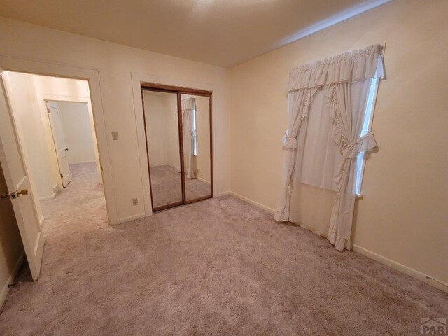 unfurnished bedroom featuring light carpet, baseboards, and a closet