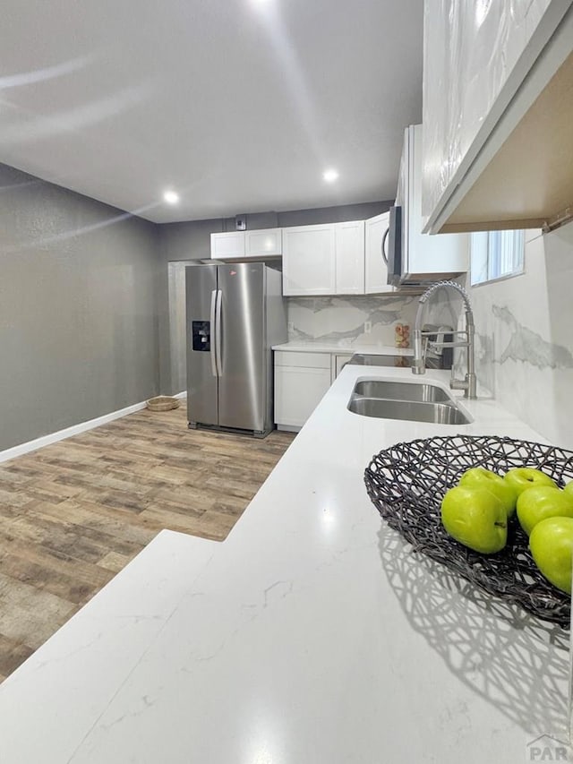 kitchen with light wood finished floors, tasteful backsplash, stainless steel refrigerator with ice dispenser, white cabinets, and a sink