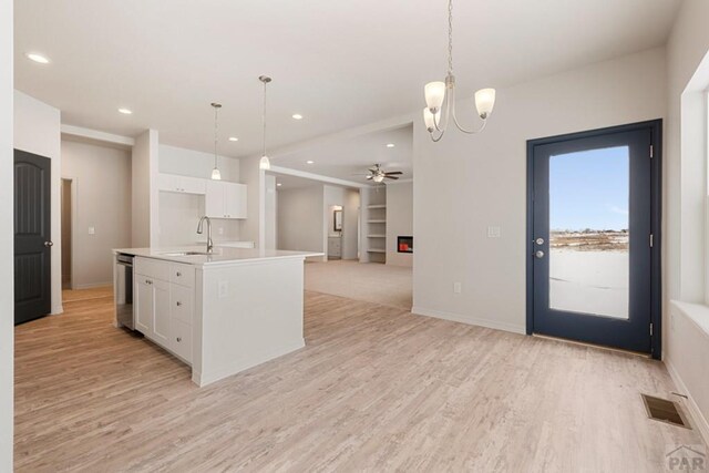 kitchen featuring white cabinets, open floor plan, a kitchen island with sink, light countertops, and pendant lighting