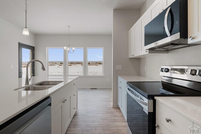 kitchen featuring a sink, white cabinetry, light countertops, appliances with stainless steel finishes, and pendant lighting