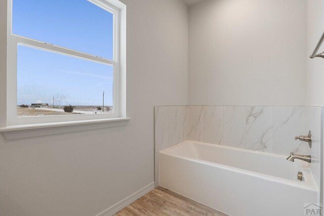 bathroom with a tub, baseboards, and wood finished floors