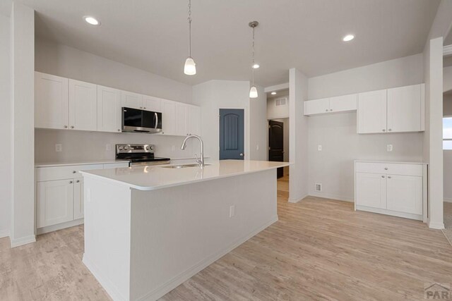 kitchen with stainless steel appliances, a sink, white cabinetry, light countertops, and a center island with sink