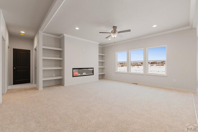 unfurnished living room with baseboards, built in features, ornamental molding, and a glass covered fireplace