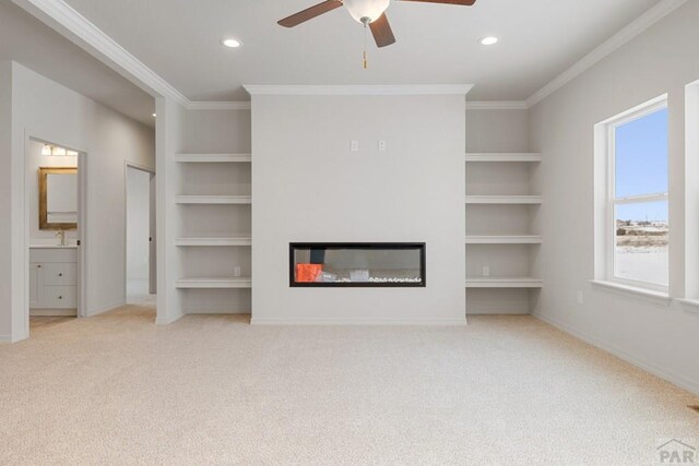 unfurnished living room featuring ornamental molding, built in shelves, and a glass covered fireplace