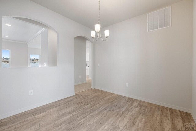 empty room with arched walkways, light wood finished floors, recessed lighting, visible vents, and baseboards