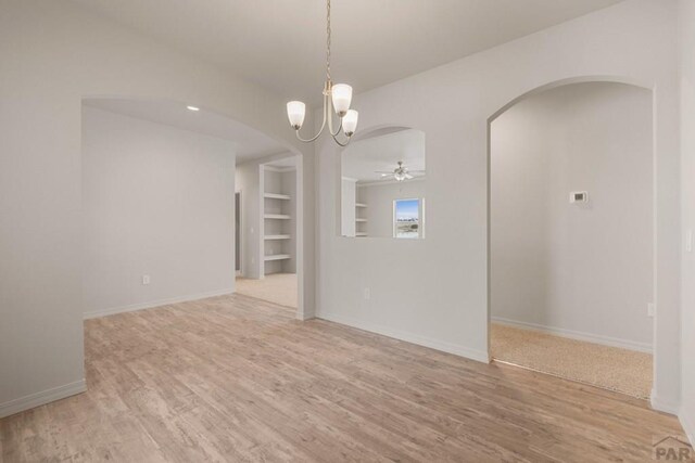 spare room featuring built in shelves, arched walkways, ceiling fan with notable chandelier, and wood finished floors