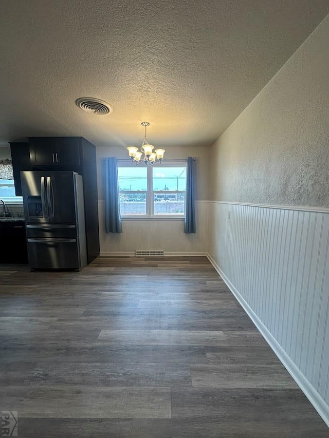 unfurnished dining area featuring a wainscoted wall, dark wood finished floors, visible vents, and an inviting chandelier