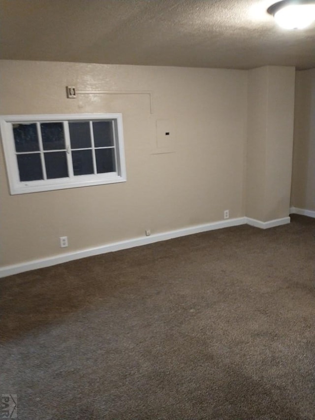 unfurnished room with a textured ceiling, dark carpet, and baseboards