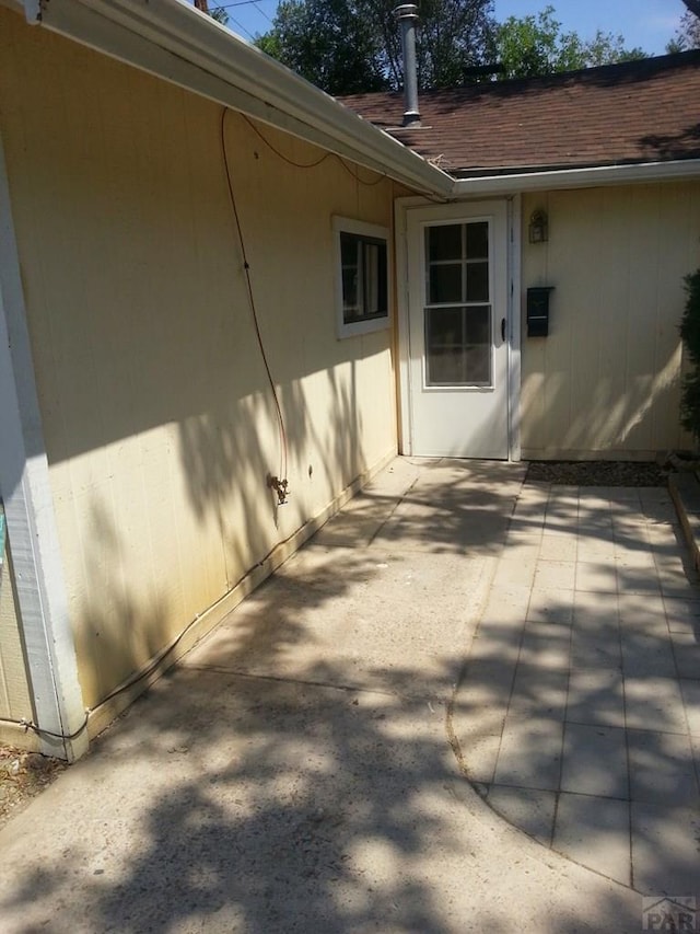 view of side of home featuring a shingled roof and a patio area