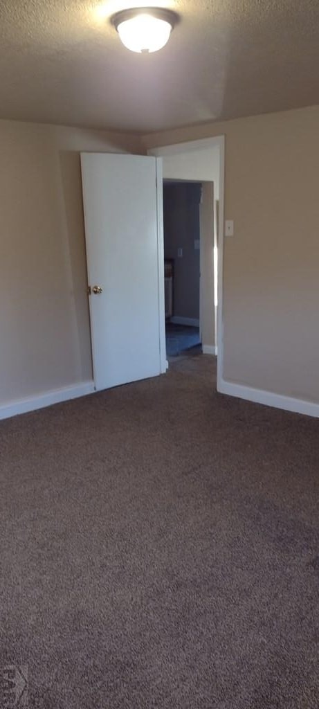 unfurnished room with baseboards, dark carpet, and a textured ceiling