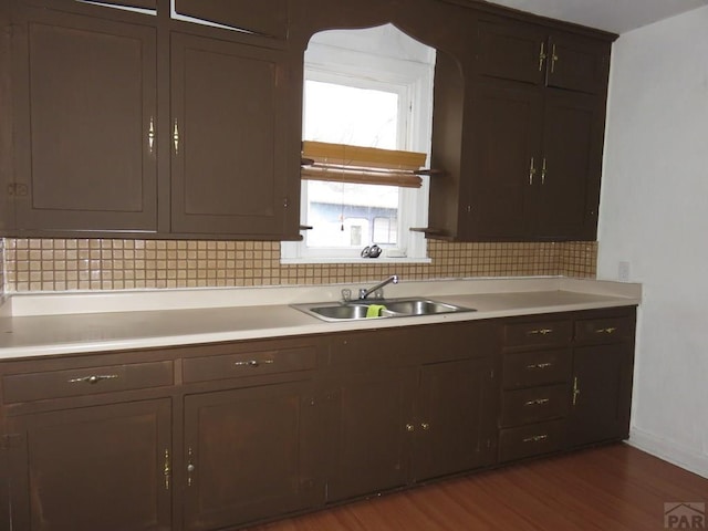 kitchen featuring dark wood finished floors, tasteful backsplash, light countertops, a sink, and dark brown cabinetry