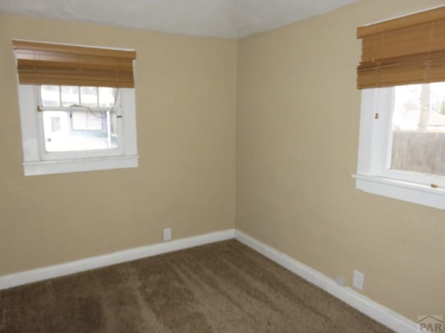 empty room featuring dark colored carpet and baseboards