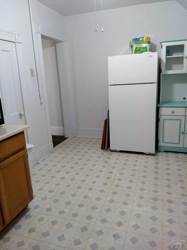 kitchen with baseboards, brown cabinetry, freestanding refrigerator, light countertops, and light floors