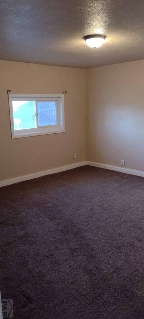 unfurnished room with dark carpet, a textured ceiling, and baseboards