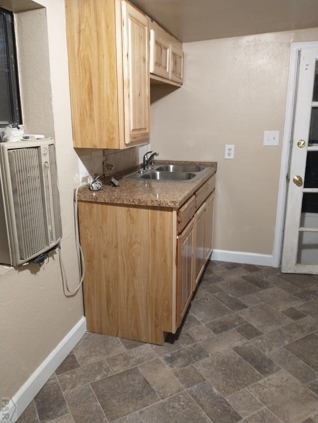 kitchen with stone finish flooring, baseboards, a sink, and light brown cabinetry