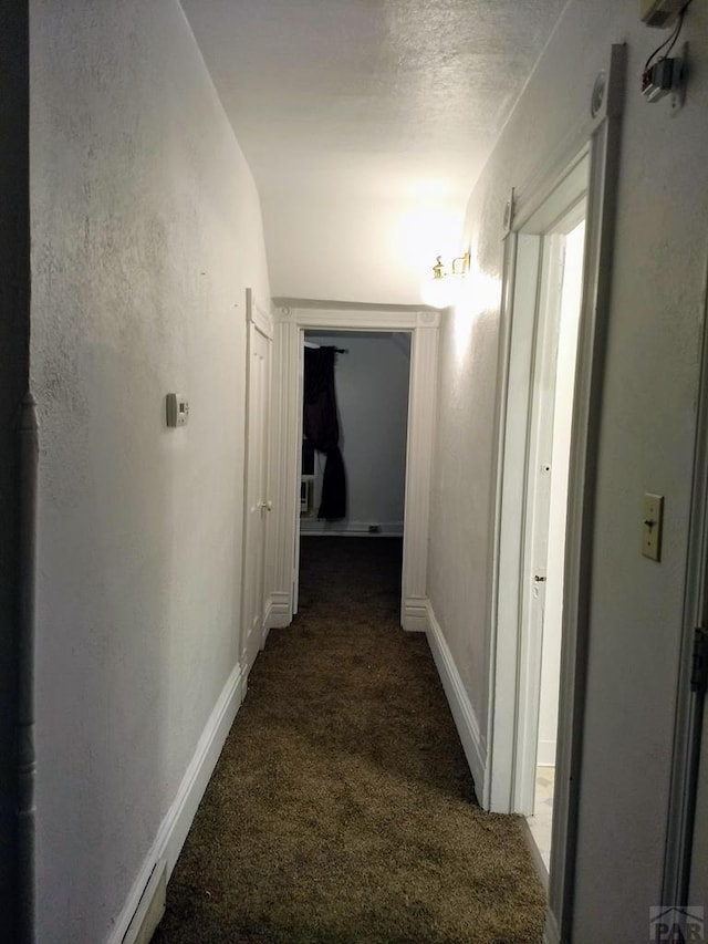 corridor featuring a textured ceiling, dark carpet, and baseboards