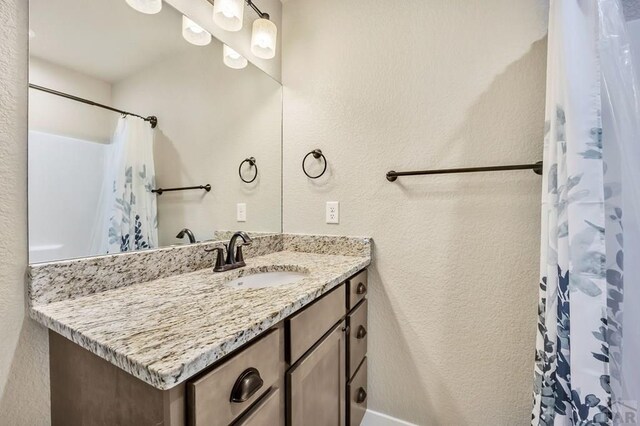 full bath with a shower with curtain, a textured wall, and vanity