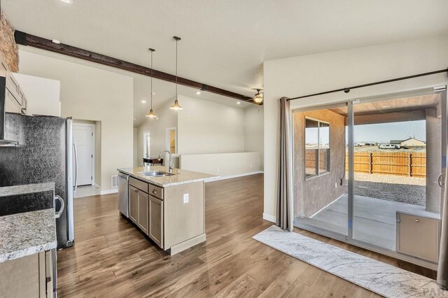 kitchen with dark wood-style floors, light stone counters, stainless steel dishwasher, pendant lighting, and a sink