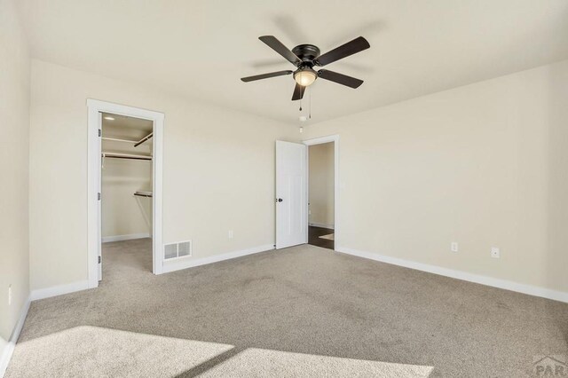 unfurnished bedroom with carpet, a walk in closet, visible vents, and baseboards