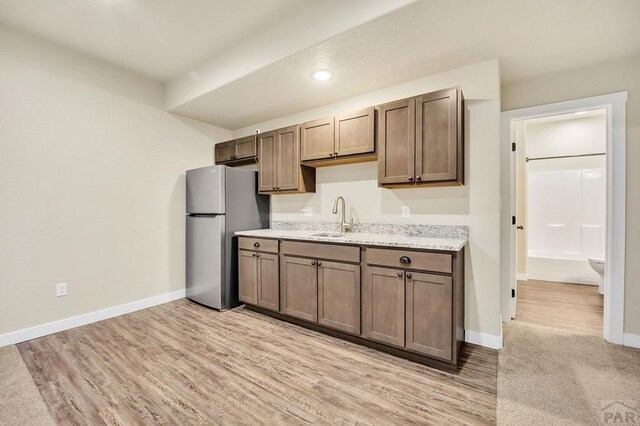 kitchen with a sink, baseboards, freestanding refrigerator, light stone countertops, and light wood finished floors