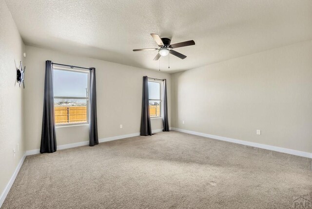 empty room featuring a textured ceiling, a healthy amount of sunlight, a ceiling fan, and light colored carpet