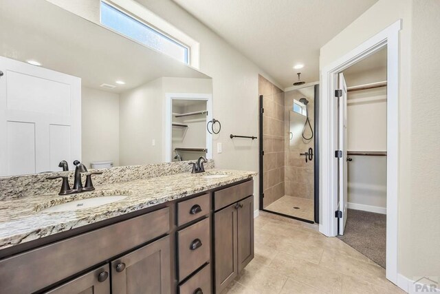 full bathroom featuring double vanity, a shower stall, a walk in closet, and a sink