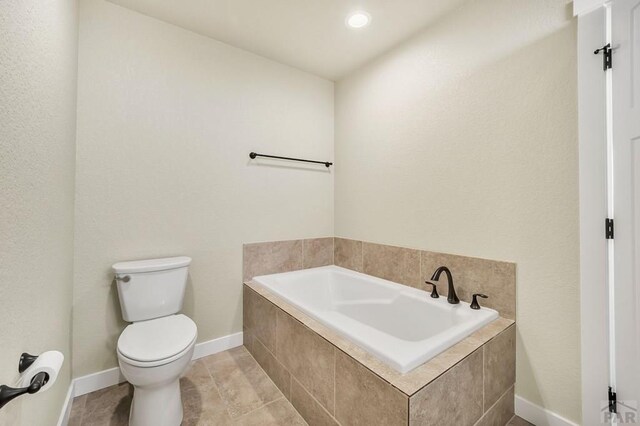 bathroom featuring tile patterned flooring, baseboards, toilet, and a bath