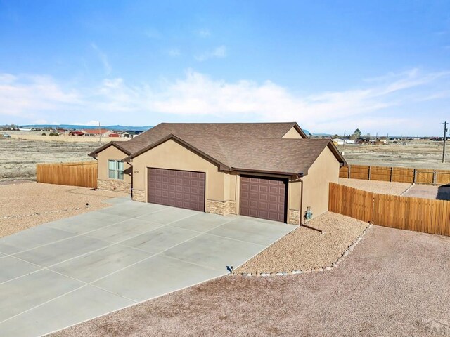 view of front facade with a garage, stone siding, fence, and stucco siding