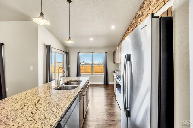 kitchen featuring light stone counters, dark wood-style flooring, decorative light fixtures, stainless steel appliances, and a sink