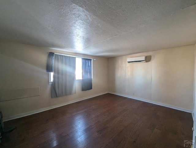 unfurnished room with a textured ceiling, dark wood-type flooring, a wall mounted AC, and baseboards