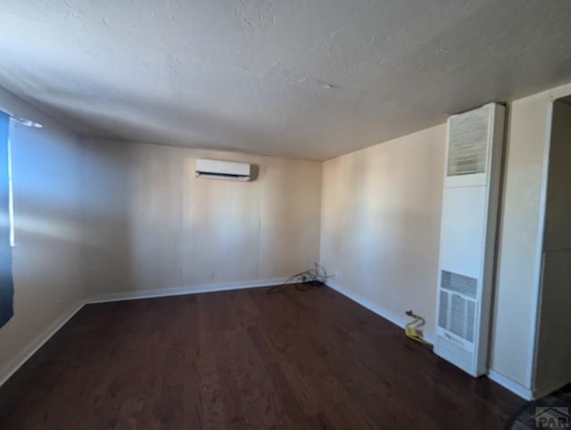 below grade area featuring a heating unit, dark wood-style flooring, a wall unit AC, and baseboards