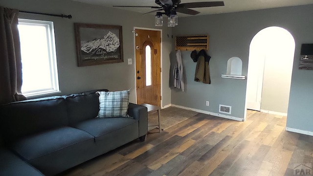 living room with arched walkways, ceiling fan, wood finished floors, visible vents, and baseboards