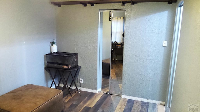 hallway with a textured wall, dark wood-type flooring, and baseboards