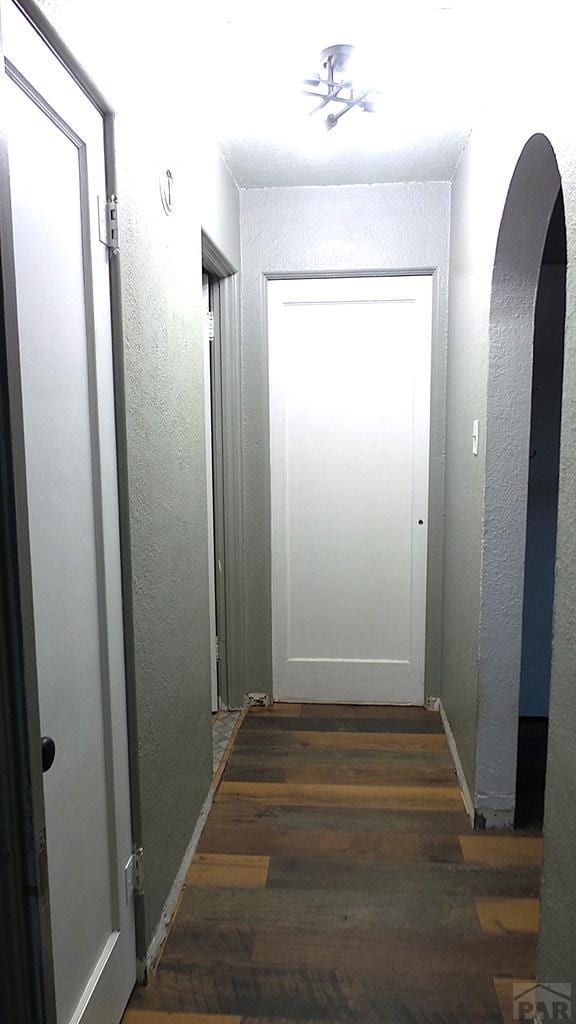 corridor featuring arched walkways, dark wood-style flooring, and a textured wall