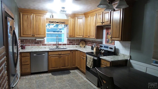 kitchen with appliances with stainless steel finishes, a sink, light stone countertops, and brown cabinets