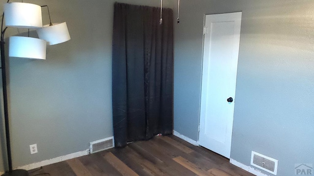 empty room with dark wood-type flooring, visible vents, and baseboards