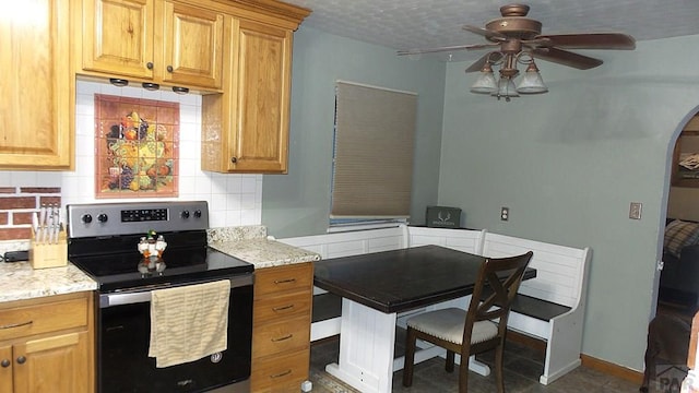 kitchen featuring arched walkways, ceiling fan, light stone counters, stainless steel range with electric stovetop, and backsplash