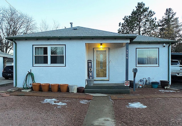 bungalow-style home featuring a shingled roof, entry steps, and stucco siding