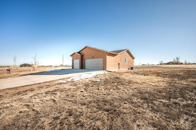 view of side of home with an attached garage, stucco siding, concrete driveway, and a rural view