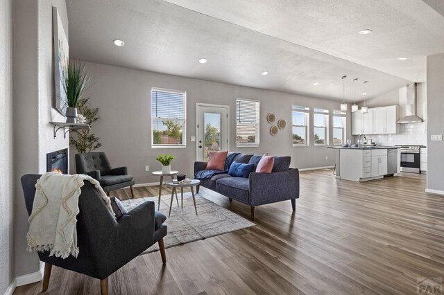 living area with light wood-type flooring, lofted ceiling, baseboards, and recessed lighting