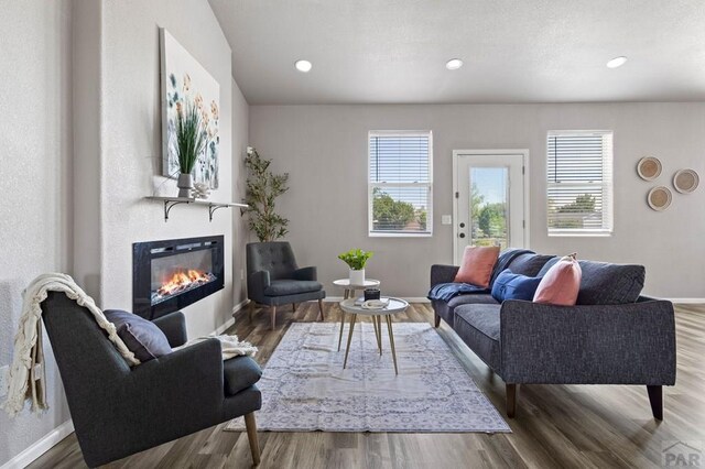 living area featuring a glass covered fireplace, recessed lighting, baseboards, and wood finished floors