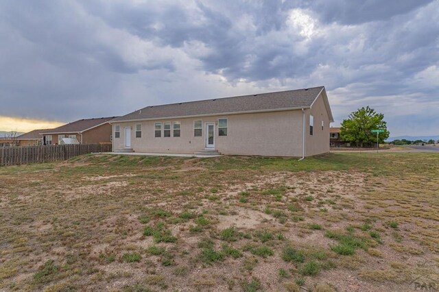 back of property featuring entry steps, a lawn, fence, and stucco siding