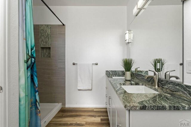 bathroom with double vanity, a sink, a shower stall, wood finished floors, and baseboards