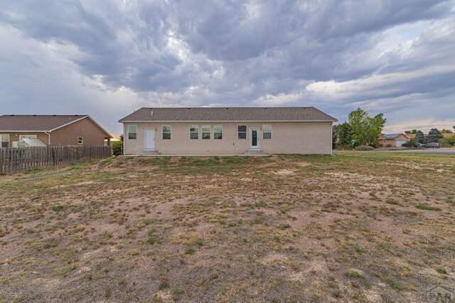 rear view of property with entry steps, fence, and stucco siding