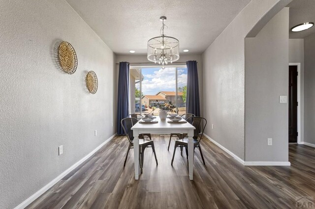 dining space with dark wood-type flooring, arched walkways, a textured wall, and baseboards