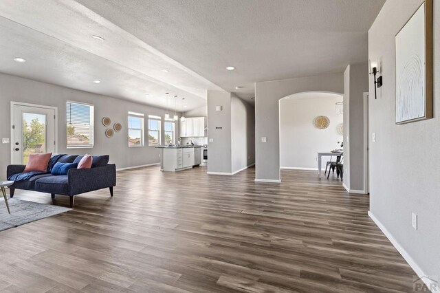 living area featuring arched walkways, dark wood-style flooring, and baseboards